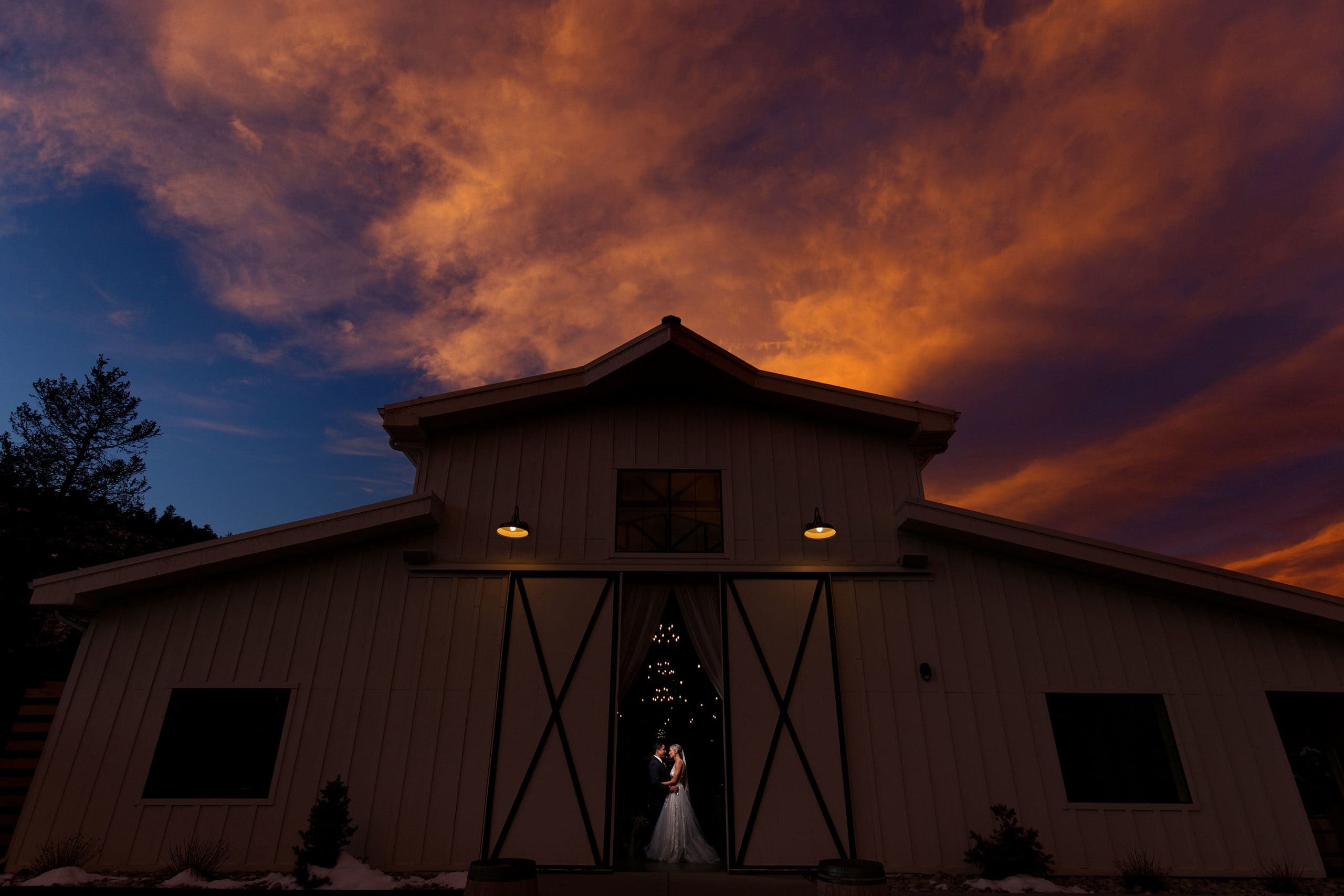Newlyweds pose between the barn doors at sunset during their wedding at Woodlands in Morrison, CO