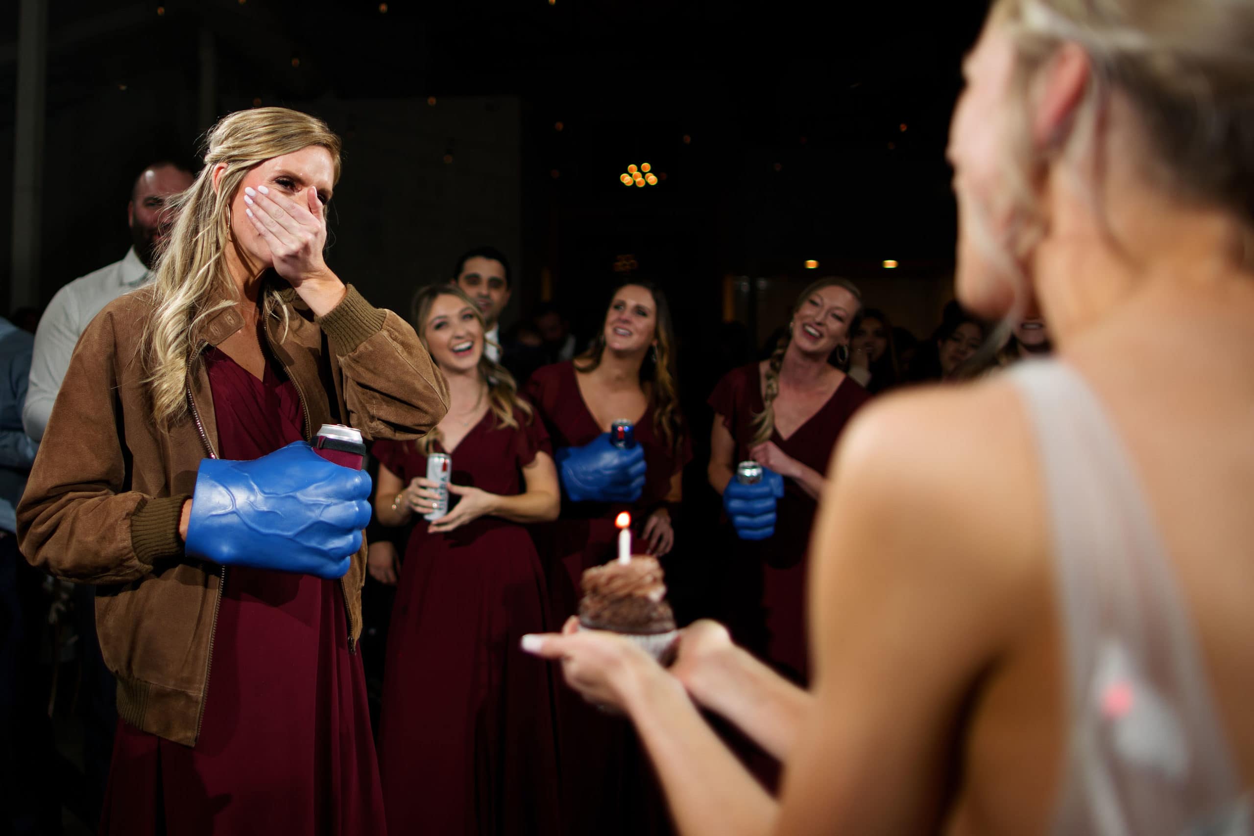 A bridesmaid reacts as the bride presents her with a candle-topped cupcake for her birthday