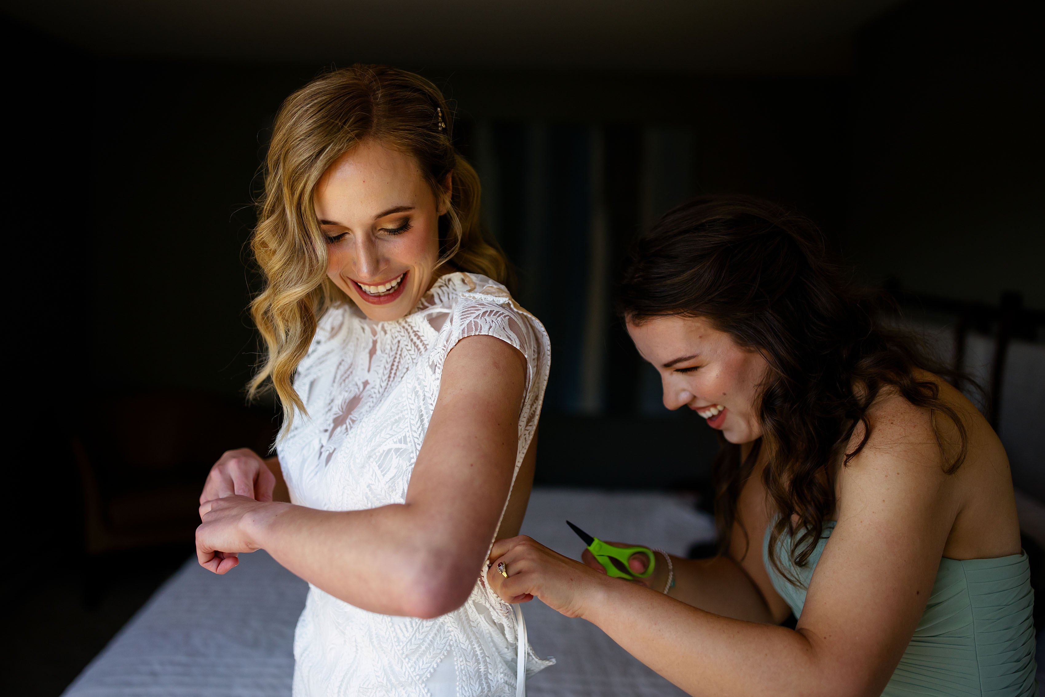 The maid of honor cuts strings off of the bride’s dress