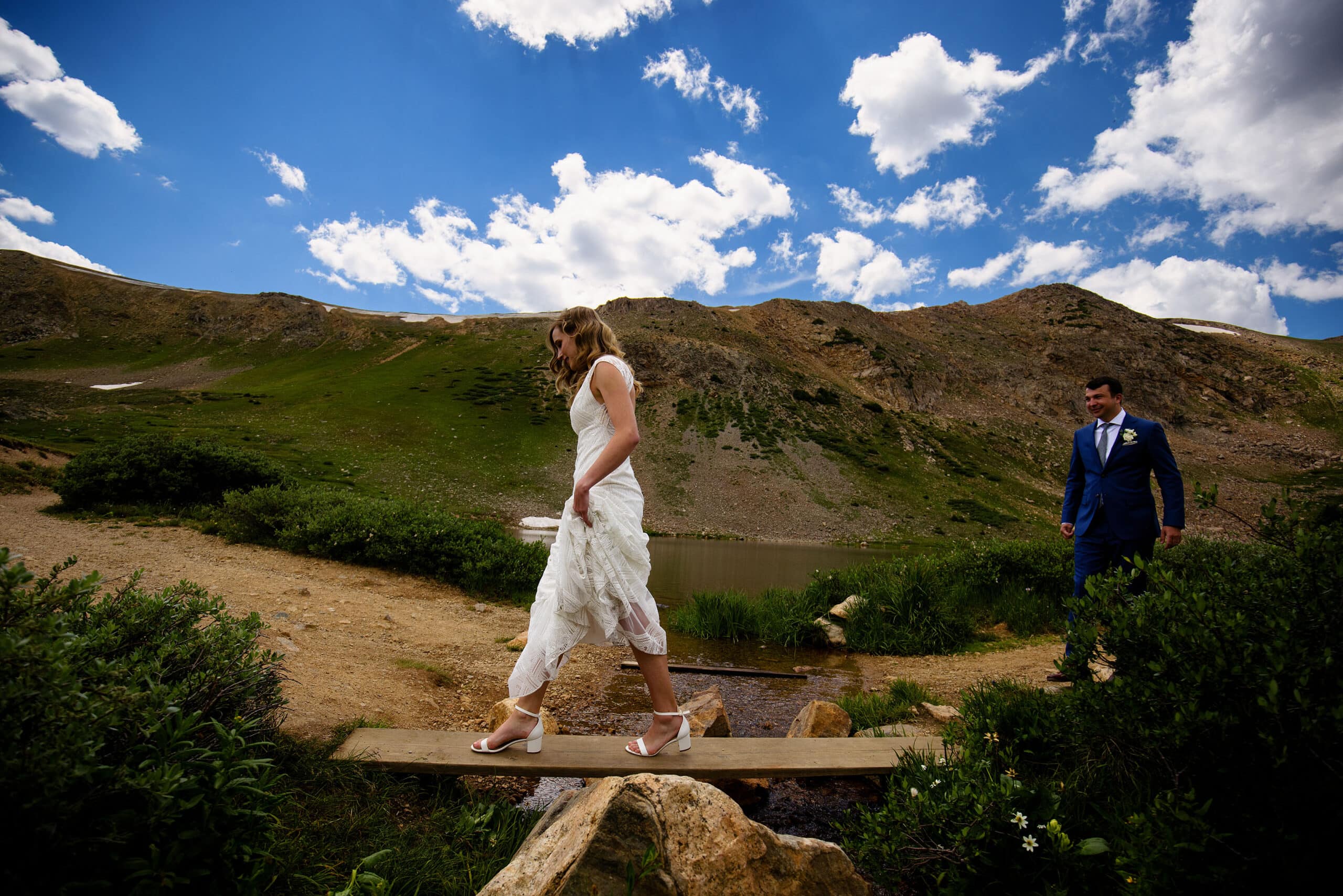 The bride crosses a stream in heels as the groom follows behind at Pass Lake