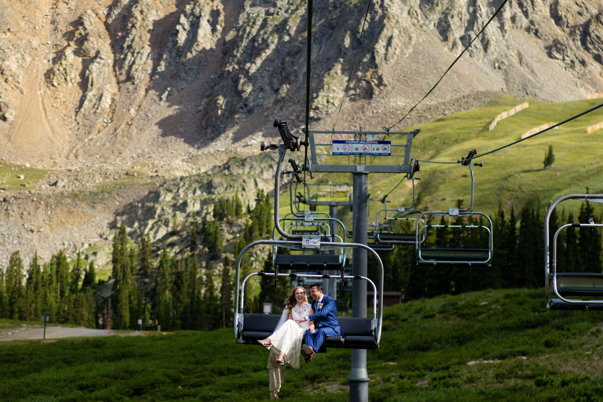 The bride and groom laugh as they ride the chairlift