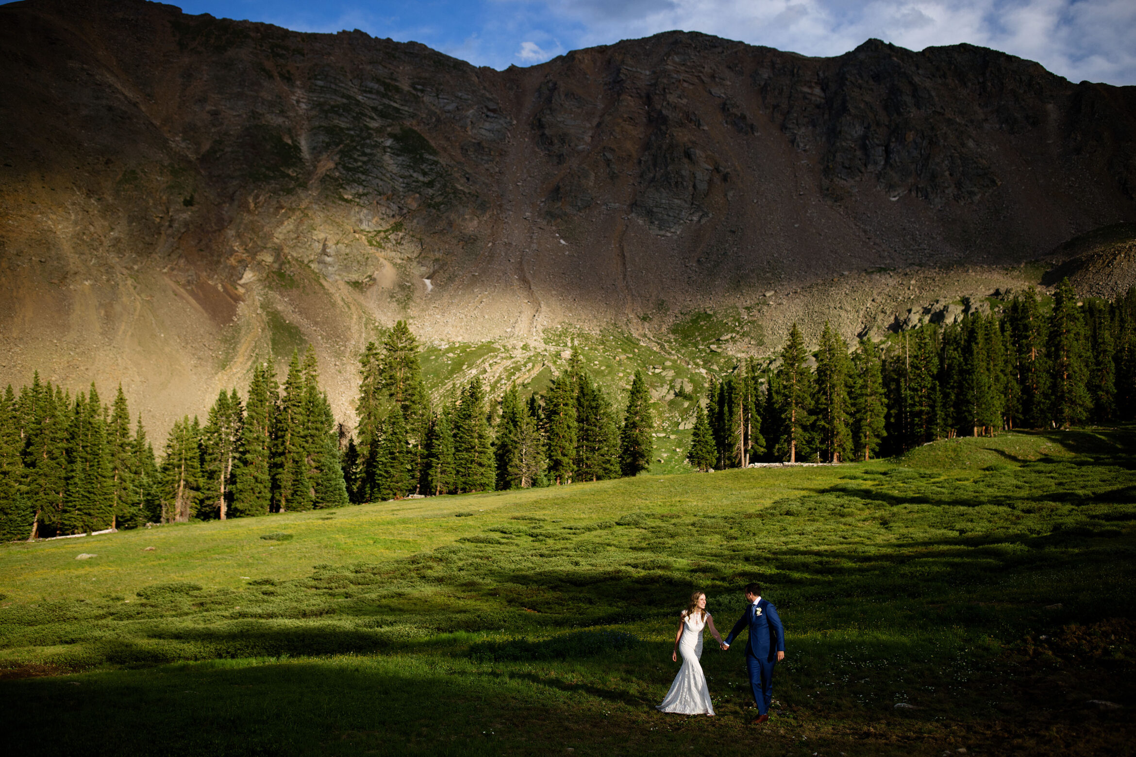 The bride and groom walk through a shaft of light at Arahoe Basin