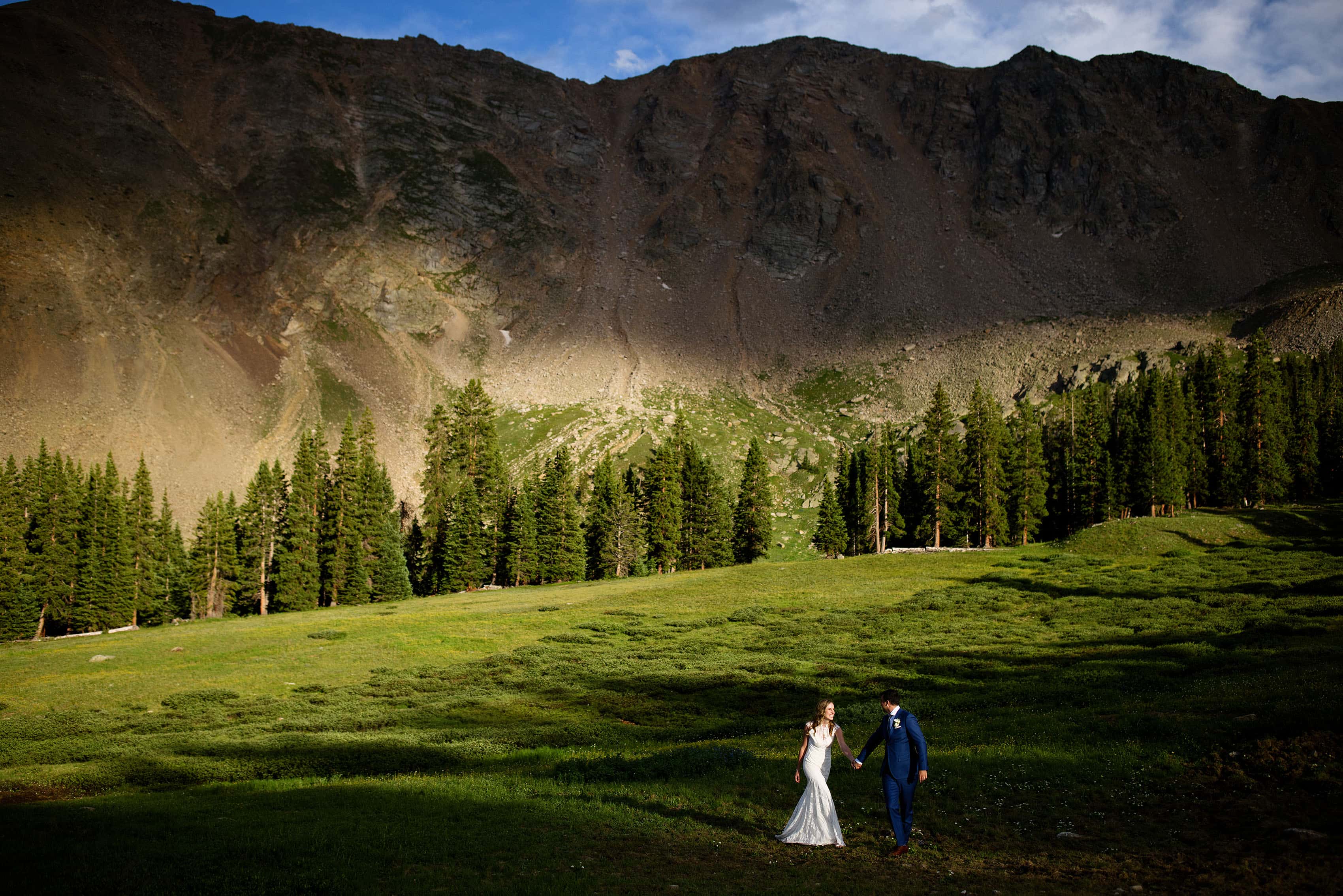 The bride and groom walk through a shaft of light at Arahoe Basin
