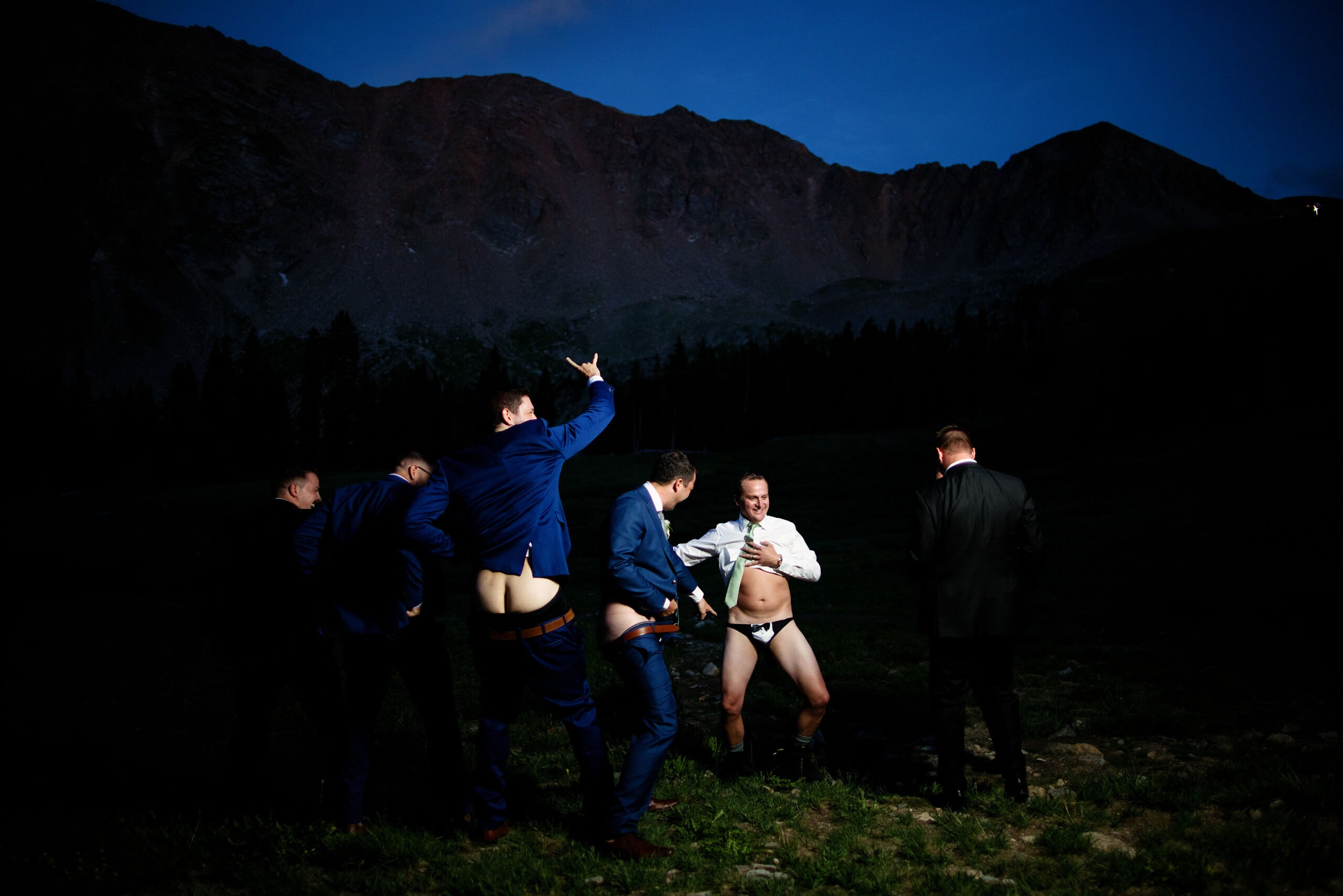 Groomsmen pose for a partially nude photo and laugh together during twilight at Arapahoe Basin