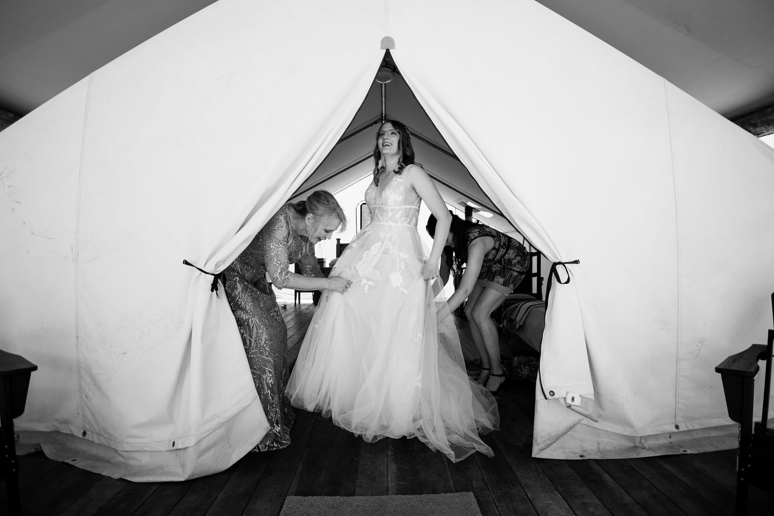 Alice gets help putting on her wedding dress in a tent at Piney River Ranch