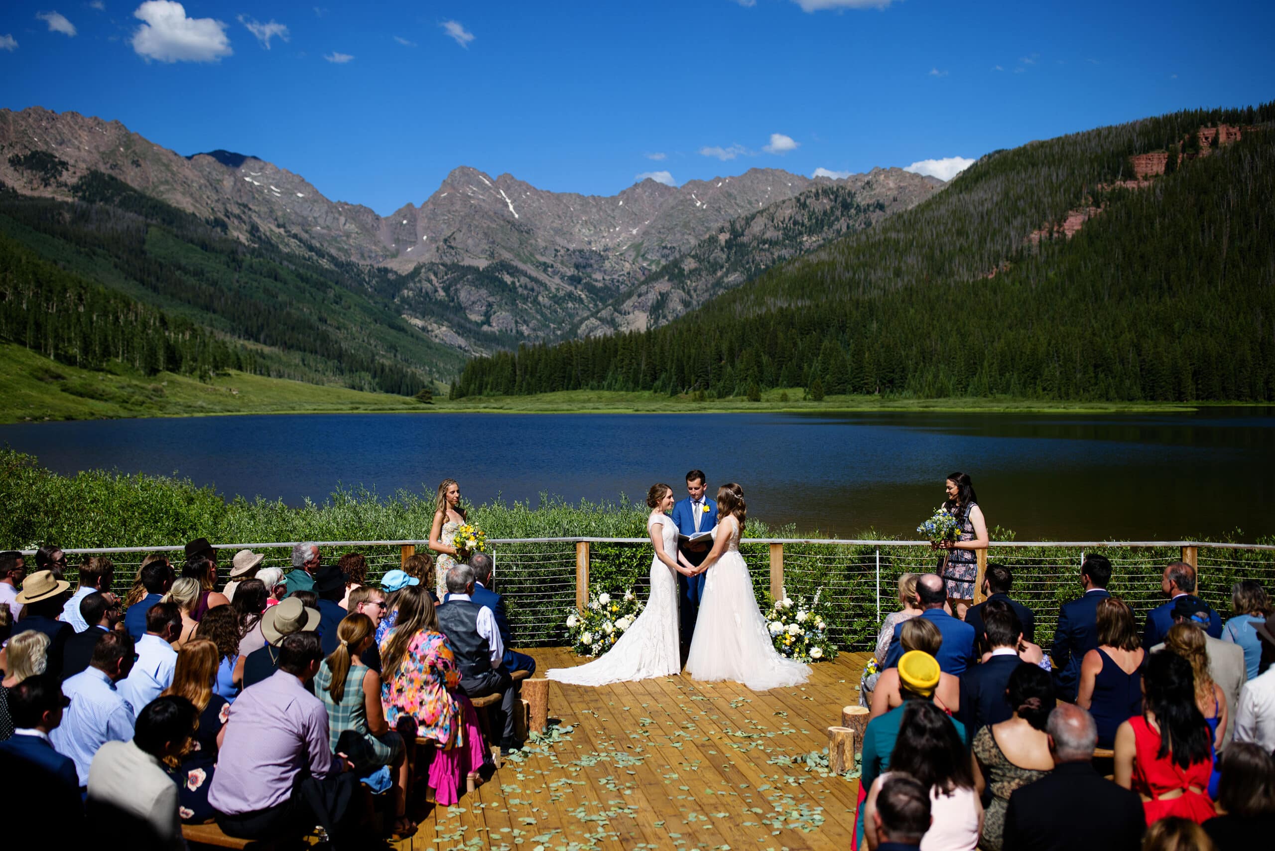 The two brides hold hands during their wedding ceremony on the deck at Piney River Ranch