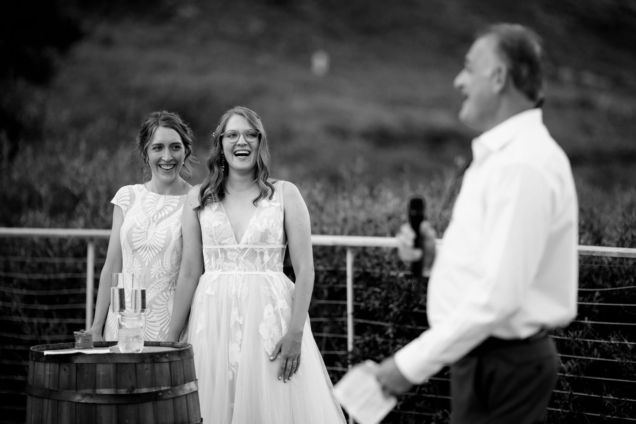 The brides laugh as a father of the bride gives a toast
