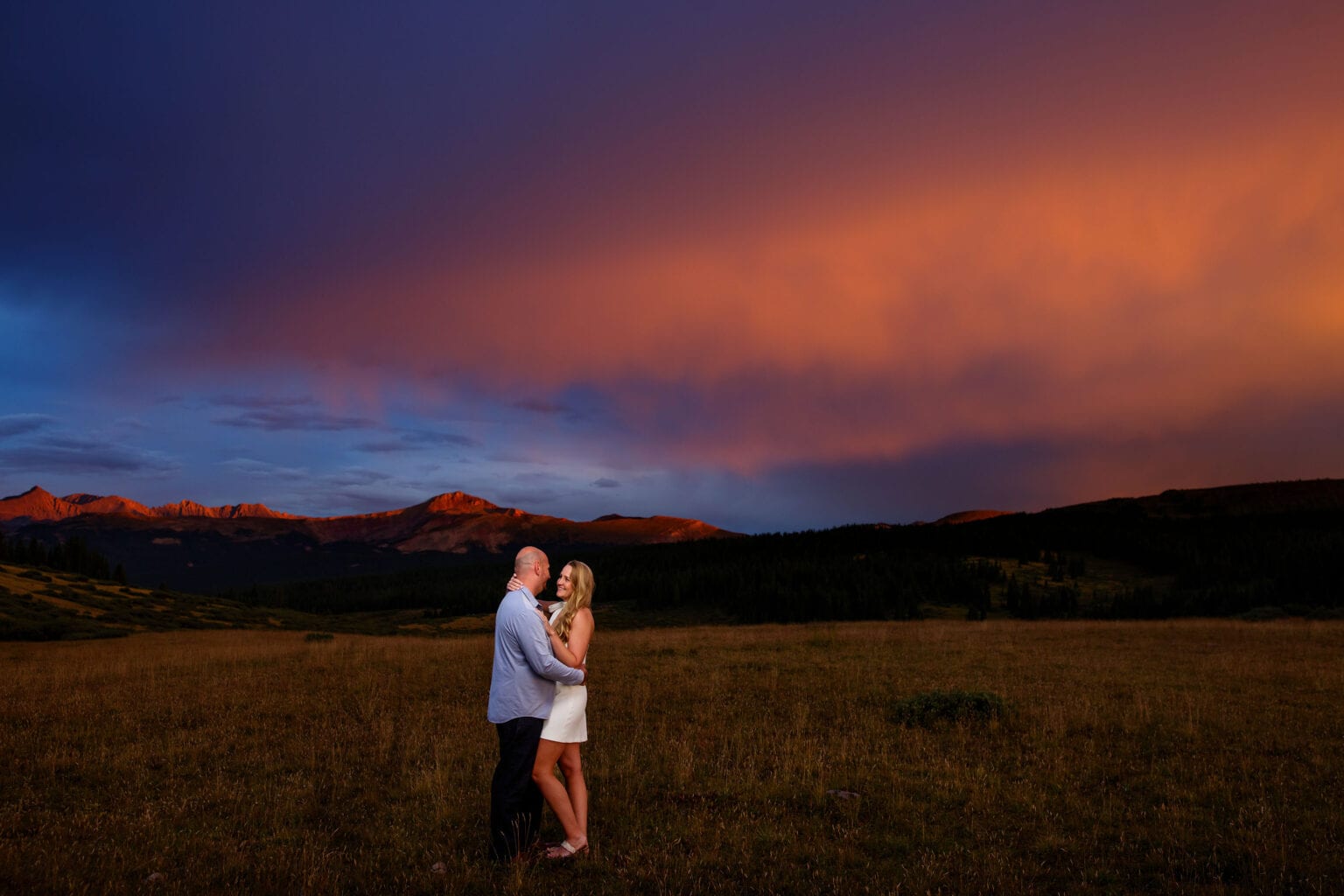 A couple poses on Shrine Pass under a cotton candy sky