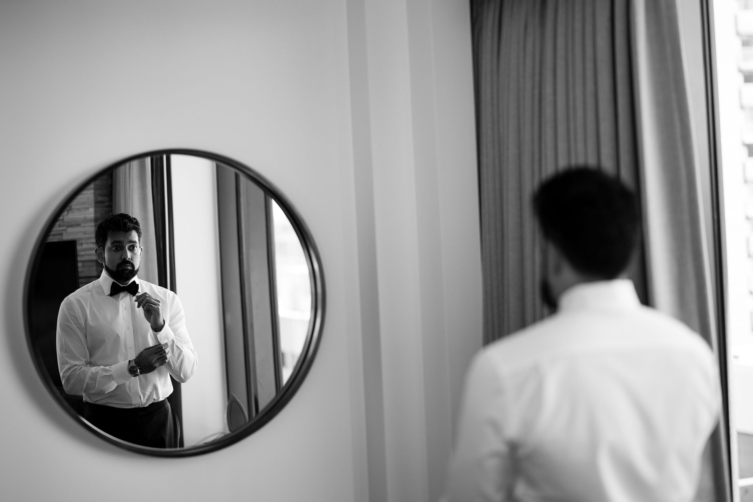 The groom buttons his sleve in a mirror