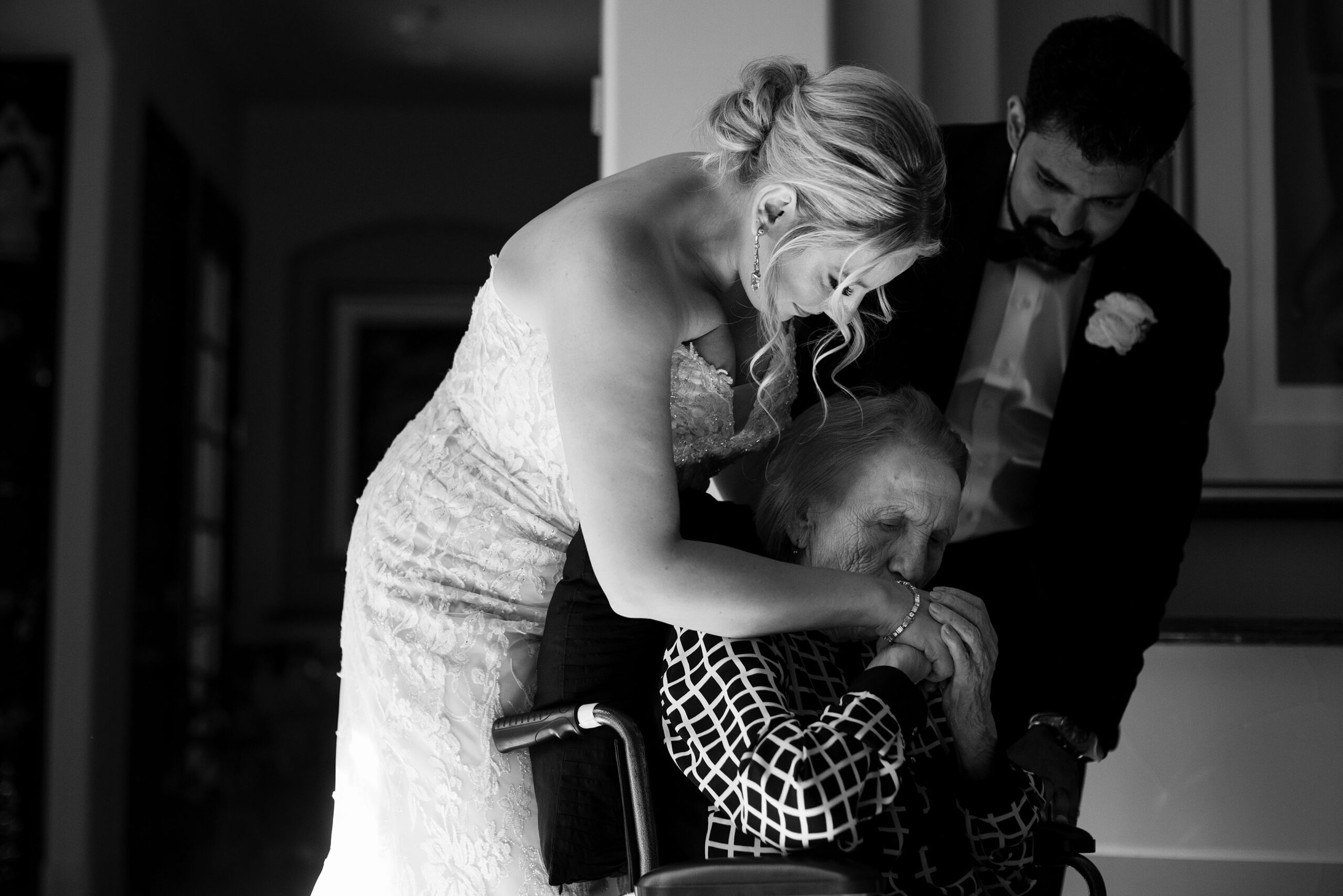 The bride receives a kiss on her hand from her grandmother as the groom looks on