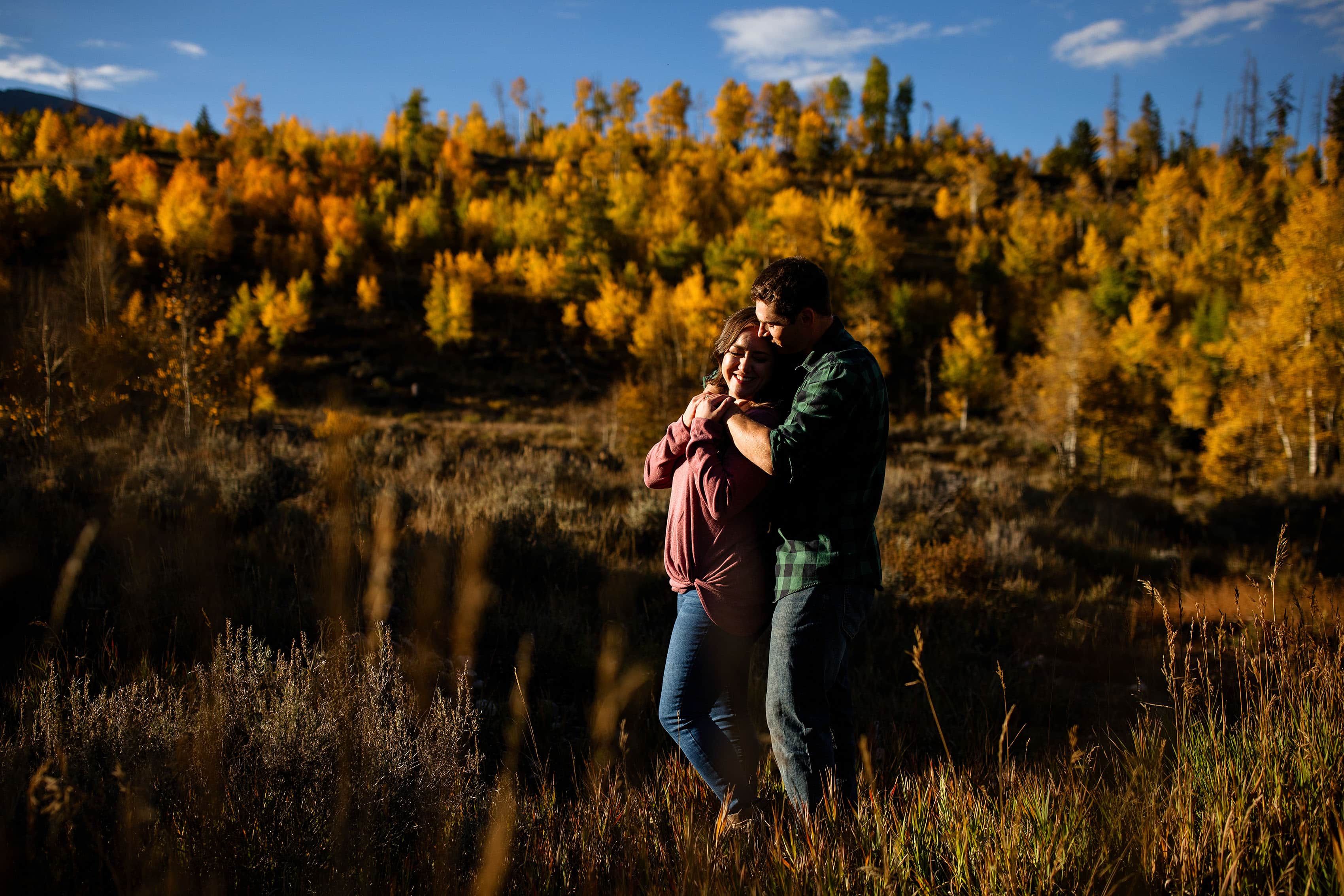 A couple embrace near a hillside of aspen trees during fall in Frisco, Colorado