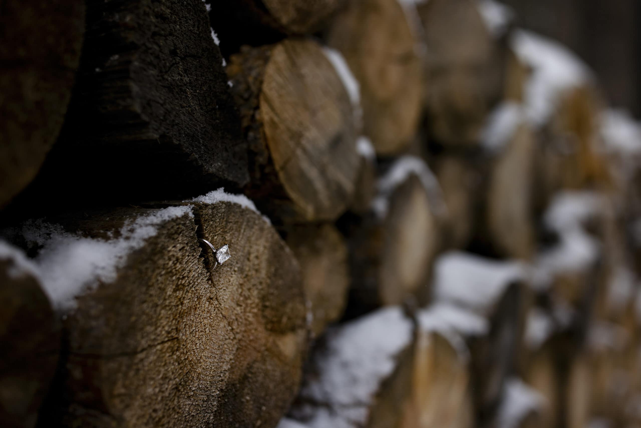 A detail of an engagement ring in a log pile during winter