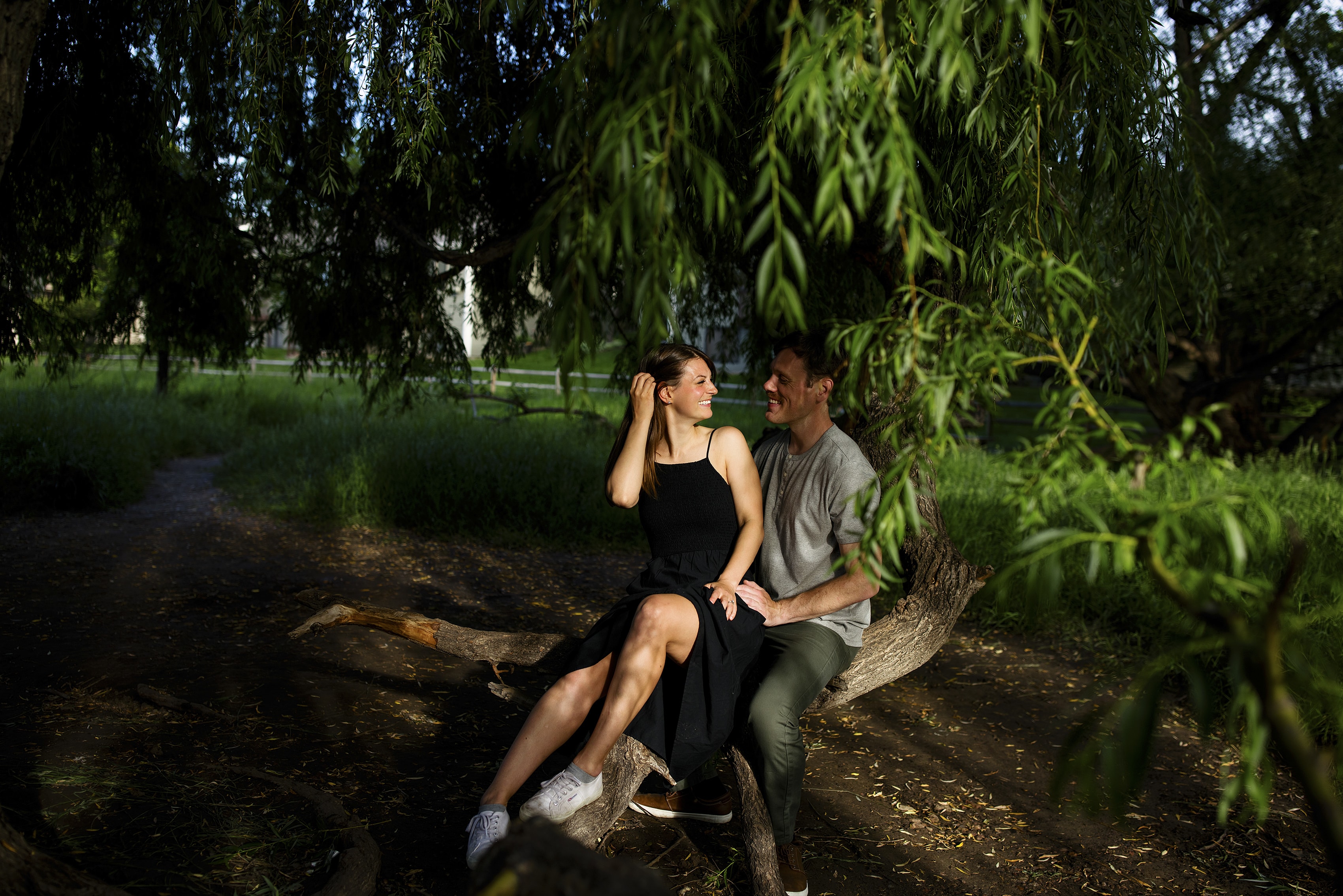 A couple sit together on a tree and smile at each other