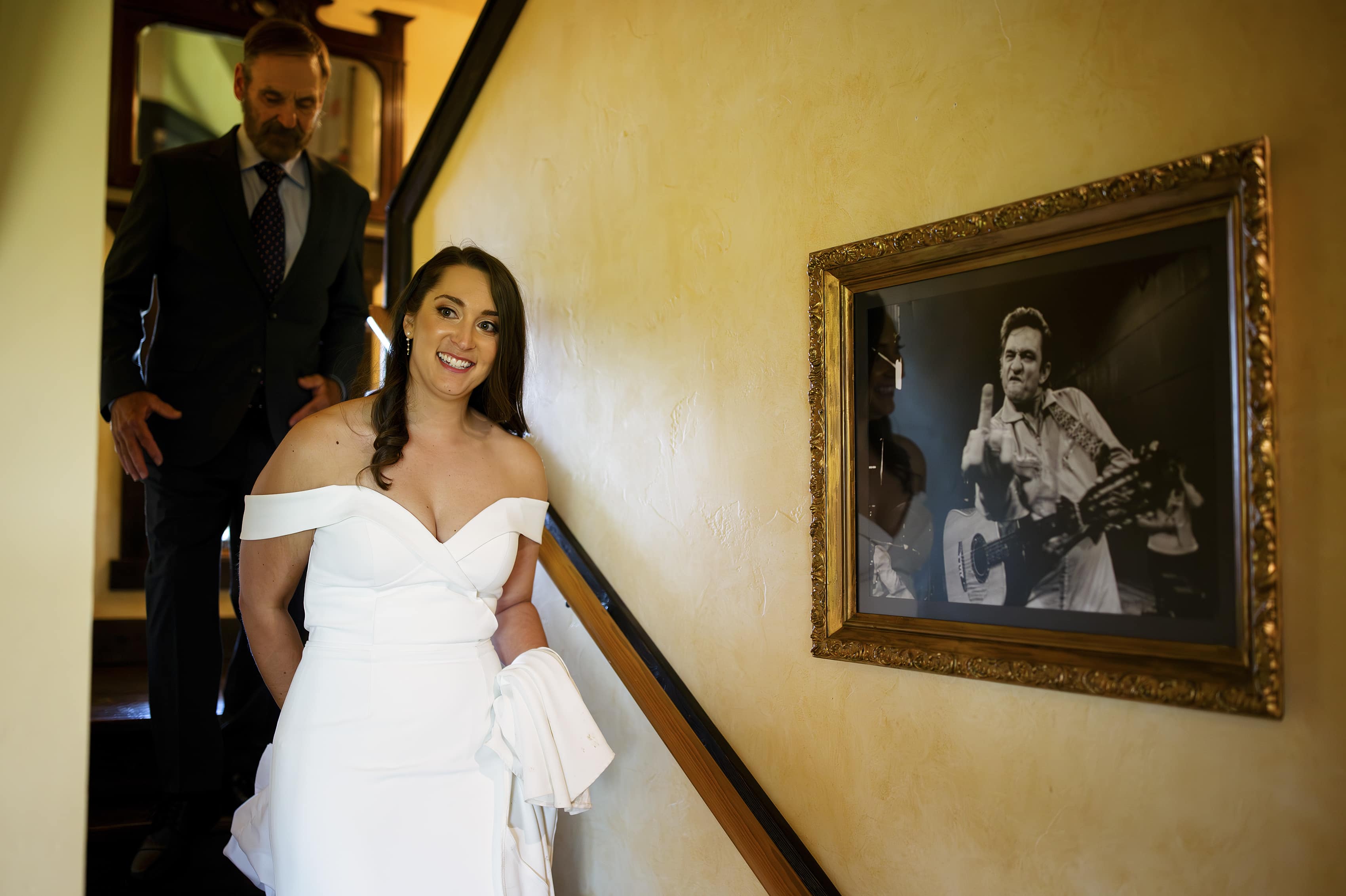 A bride walks down the stairs past a rock and roll portrait on the wall