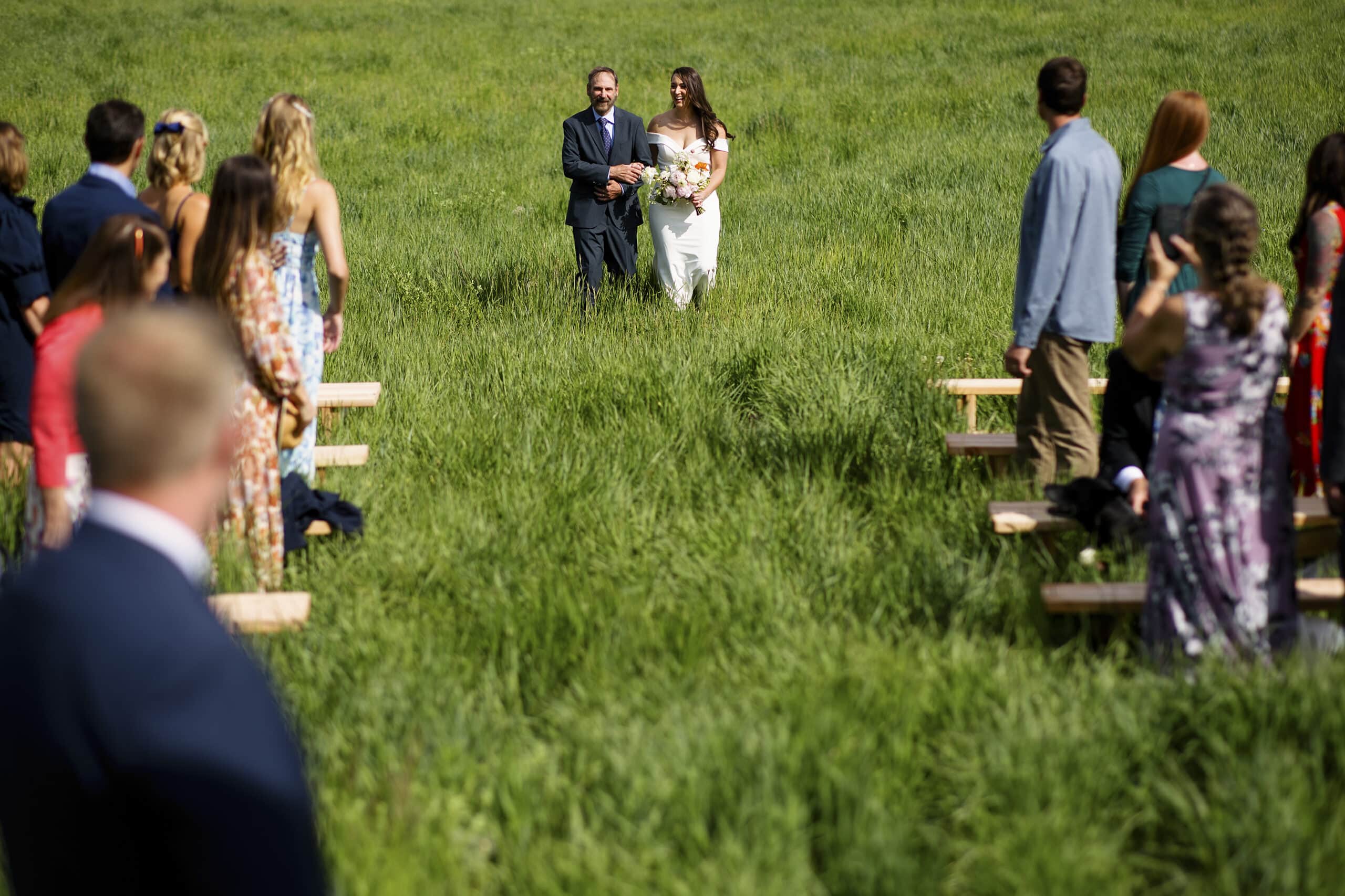 The bride and her father walk down an aisle of tall grass