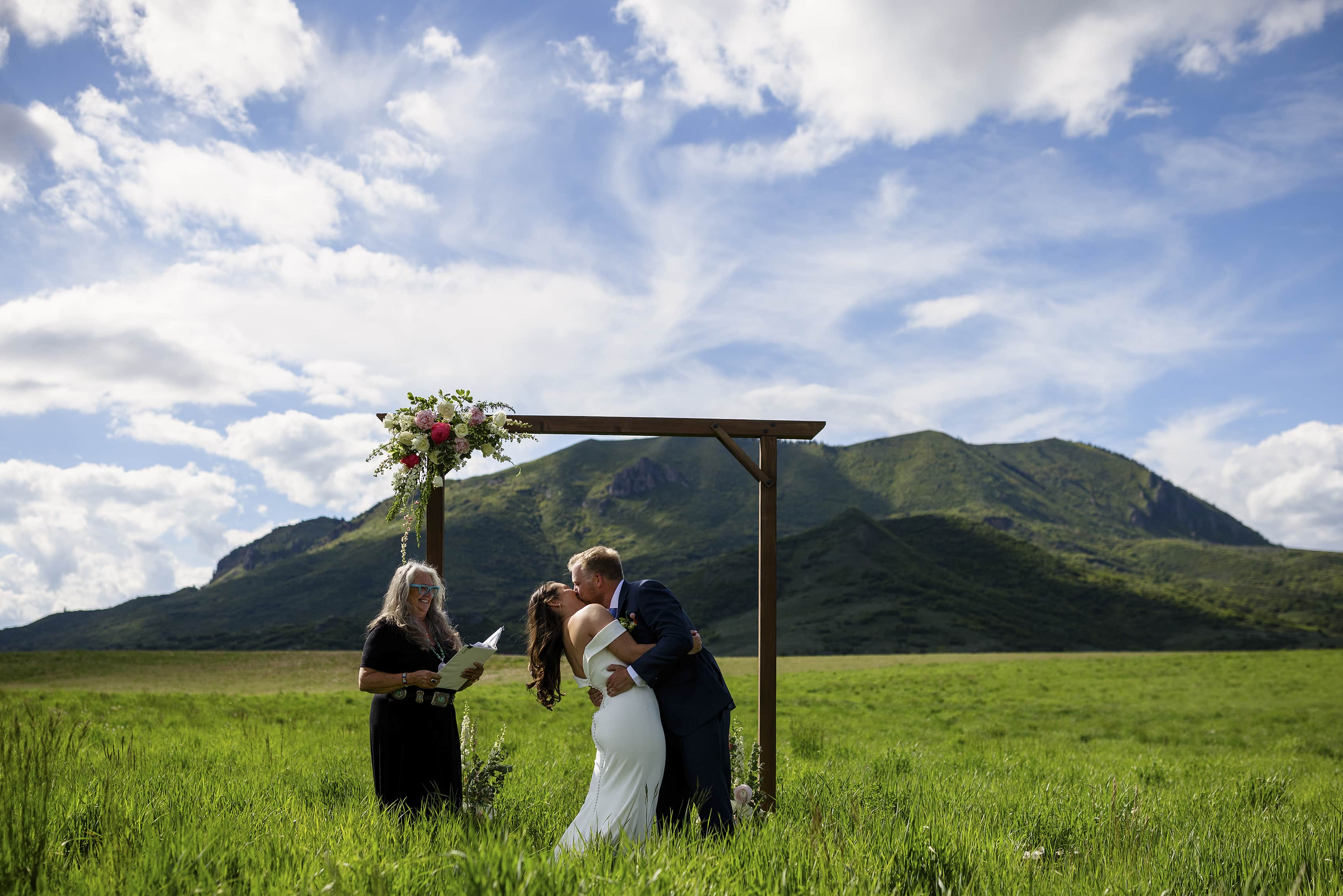 The bride and groom share their first kiss under an arbor with Elk Mountain in the background in Steamboat Springs