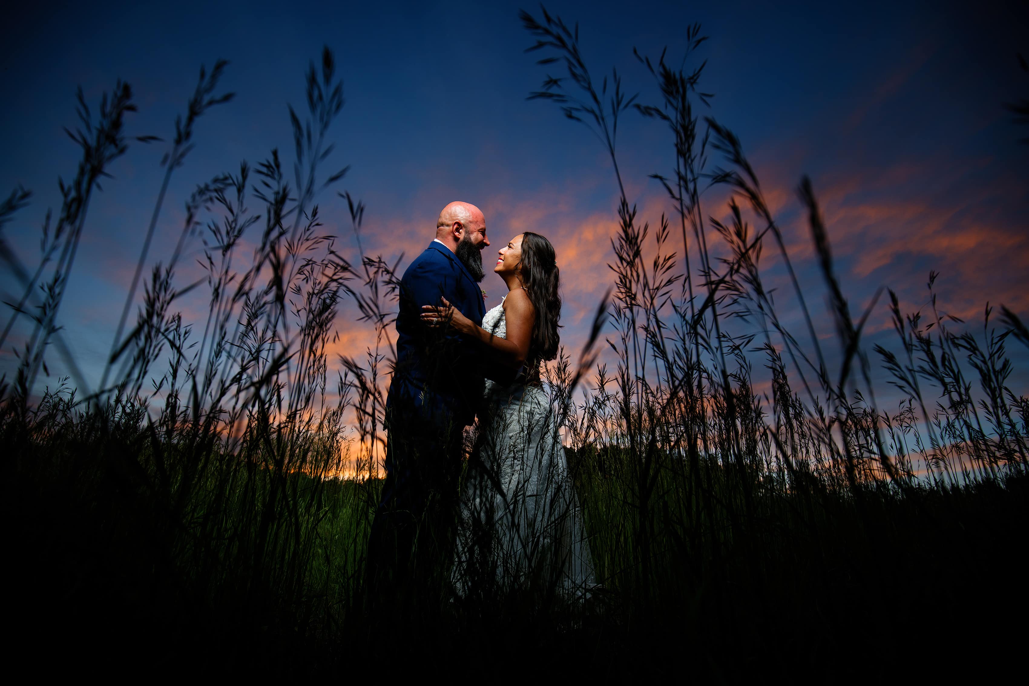 Newlyweds pose in the tall grass as the sun sets behind them at Younger Ranch in Colorado Springs