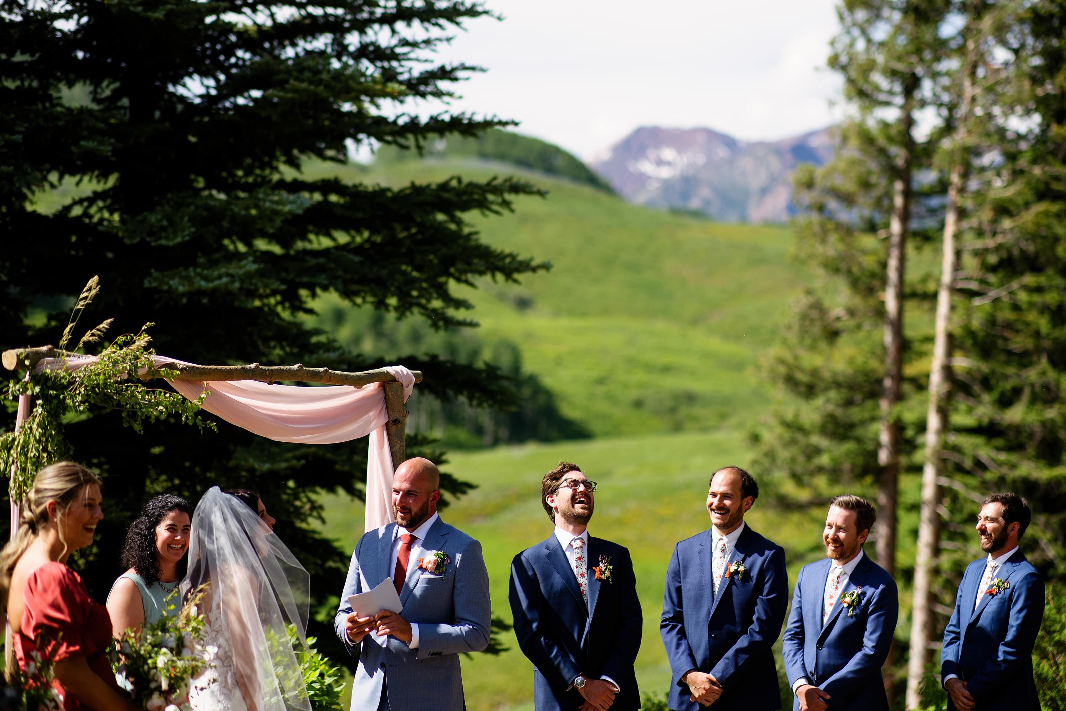 The groom reads his vows as the bride and groomsmen laugh