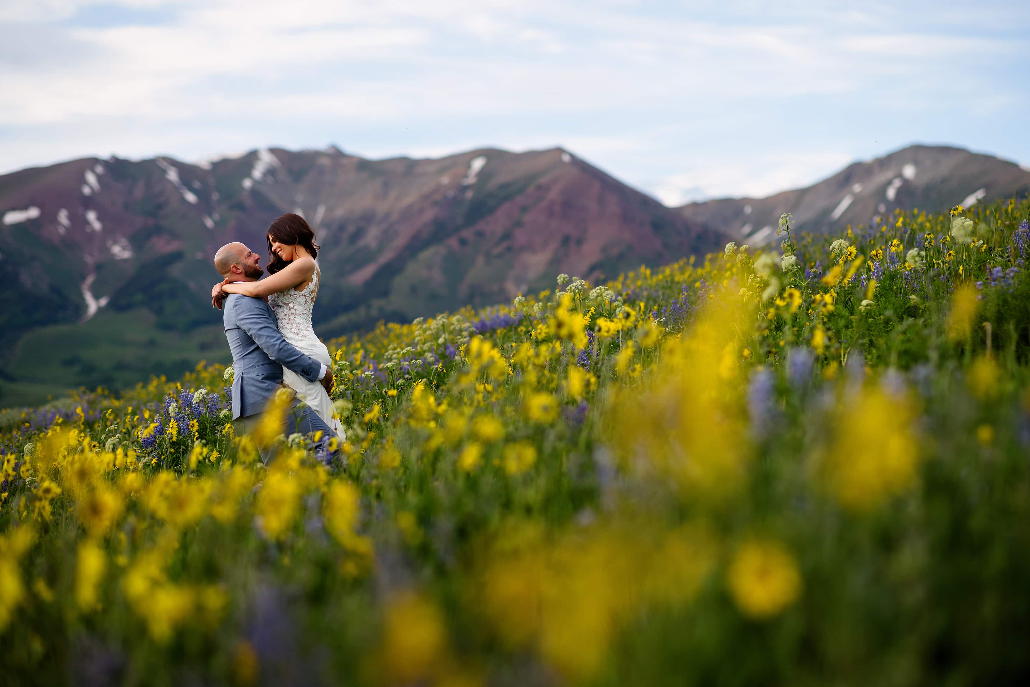 Michael and Sarah embrace on the side of a mountain in a field of daises in Crested Butte