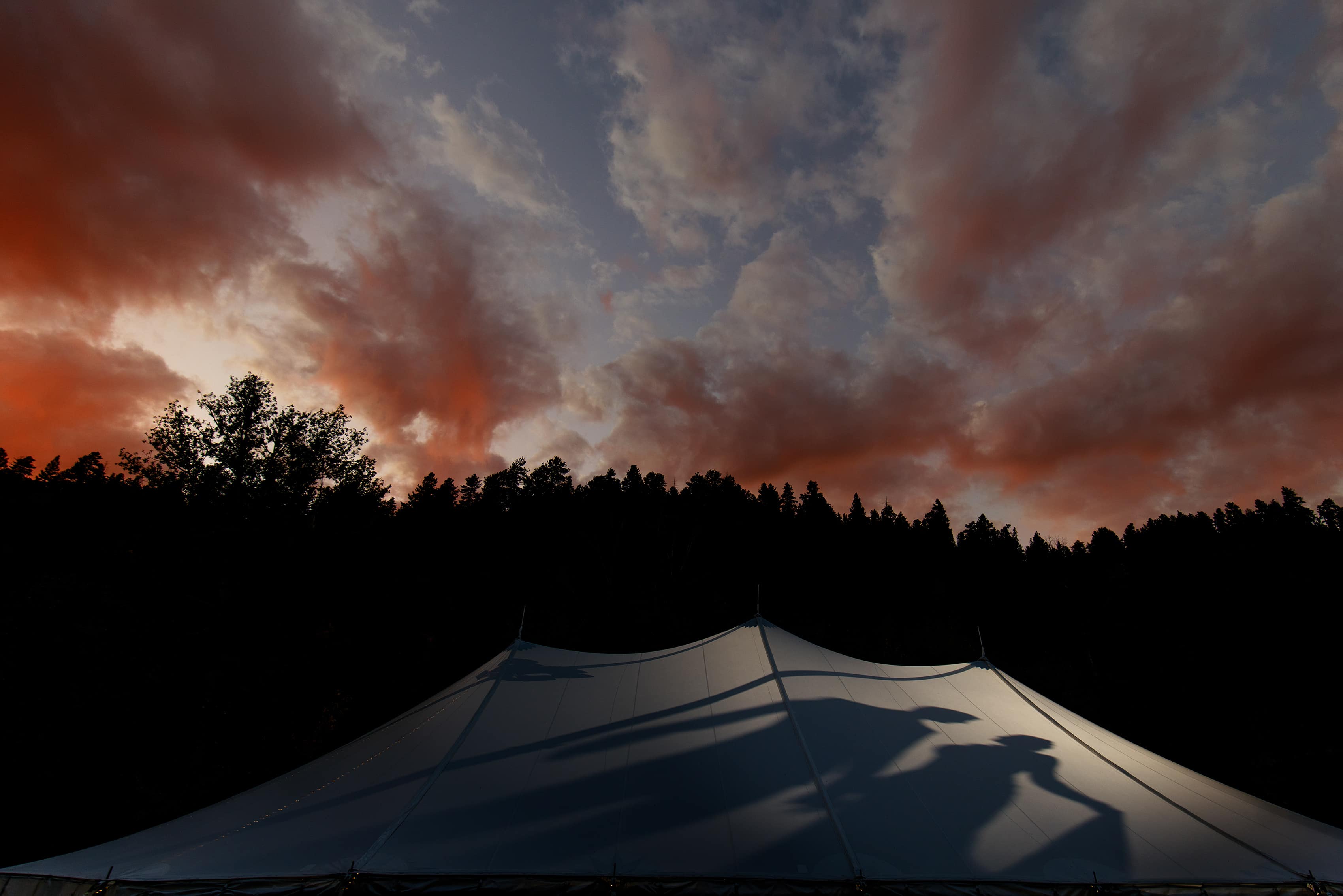 A couple is silhouetted against the wedding tent during their first dance as the sun sets above them