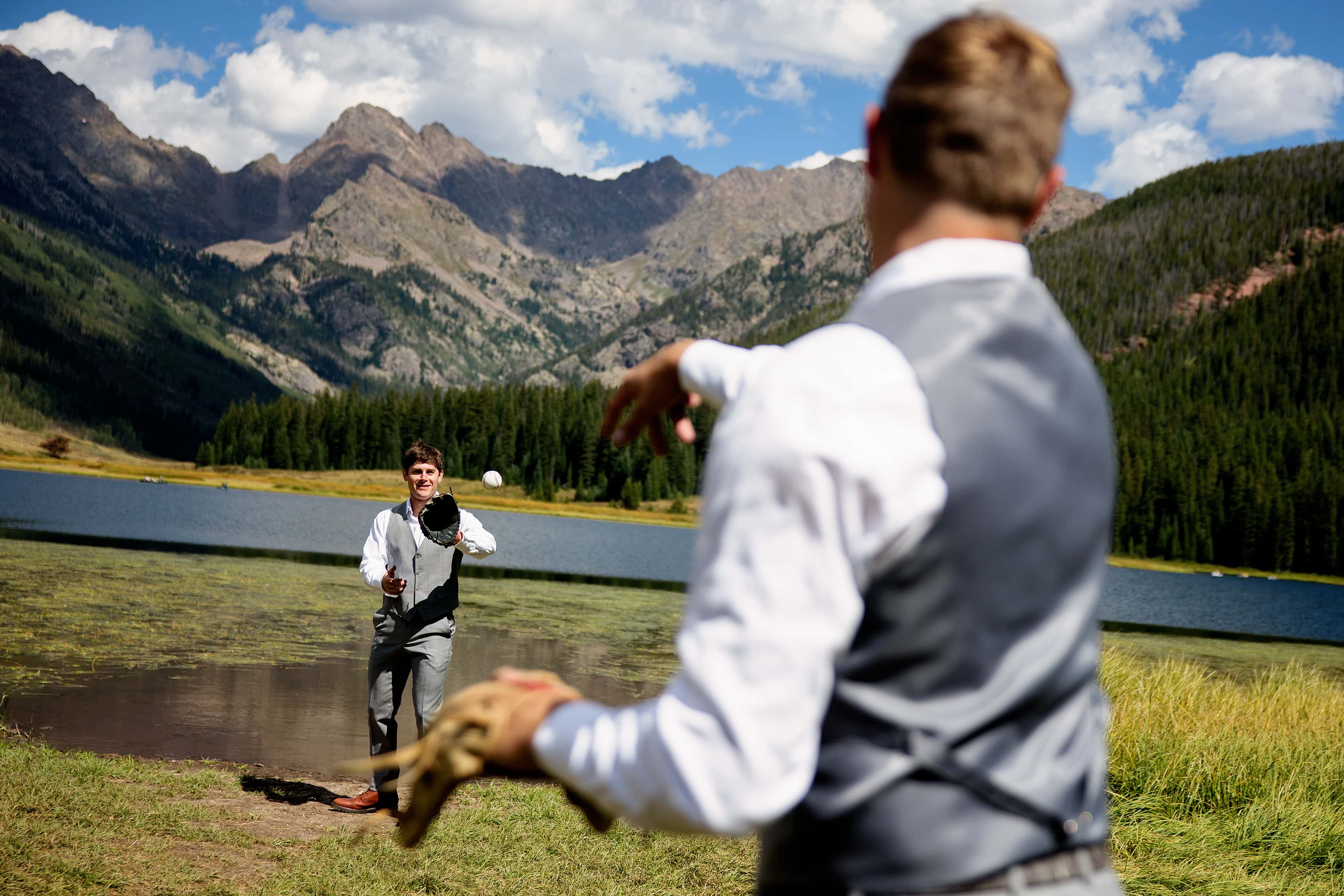 The groom plays catch near the water’s edge with a groomsman at Piney Lake on his wedding day