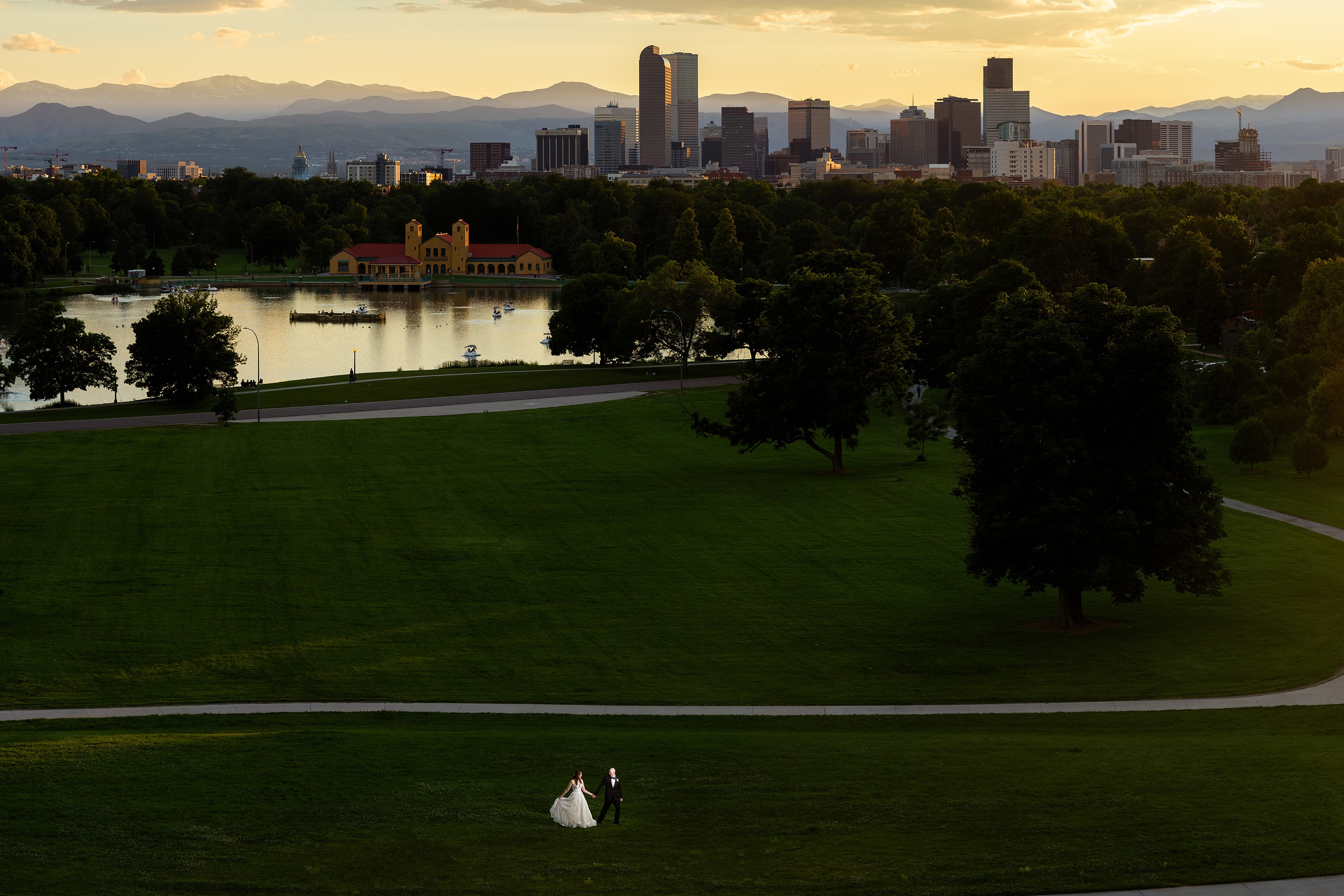 The bride and groom walk together in the grass in City Park outside the Denver Museum of Nature and Science as the sun sets behind the skyline and mountains